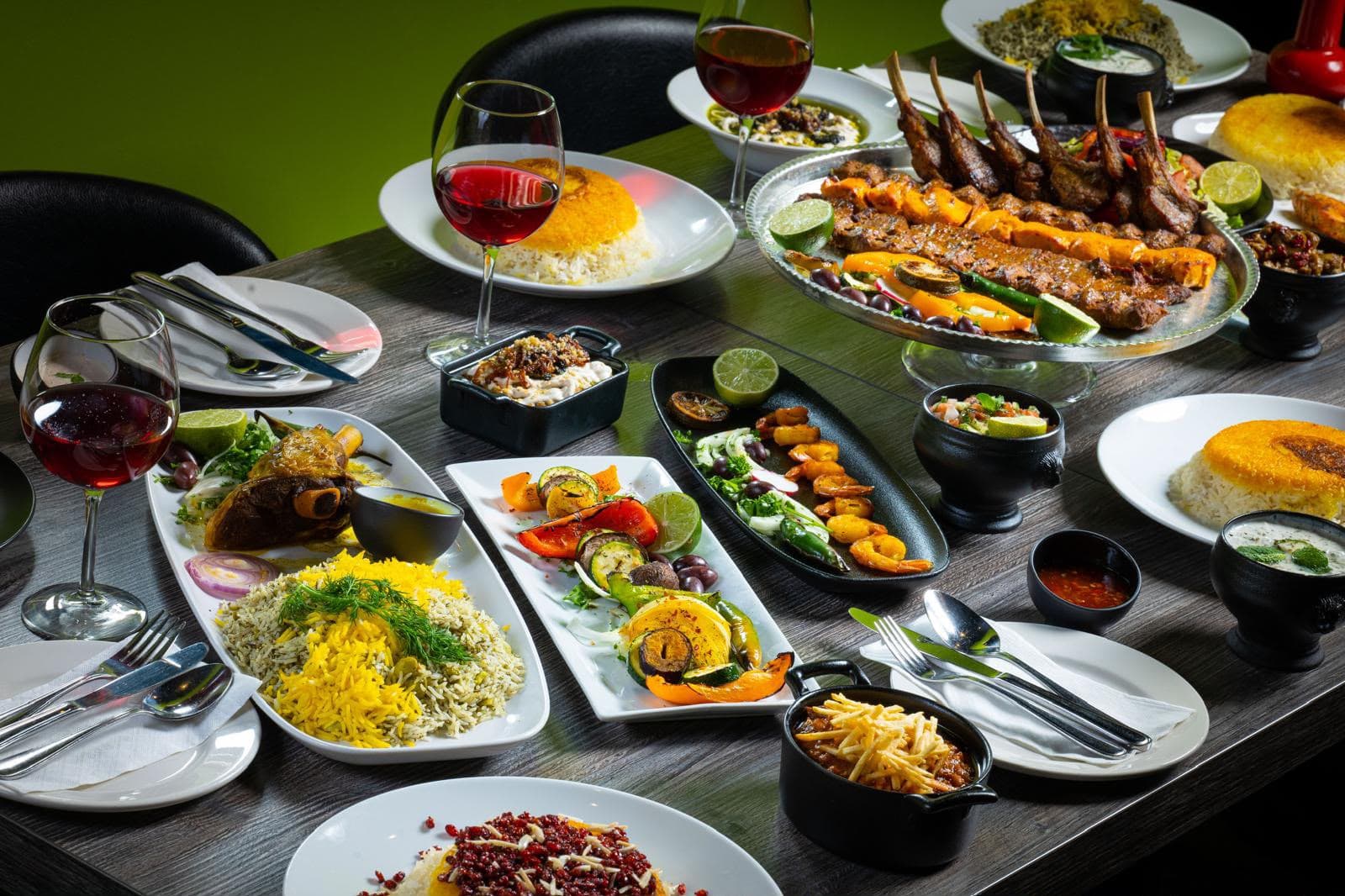 A full spread of Persian dishes, kebab platter, saffron rice, and wine on a table